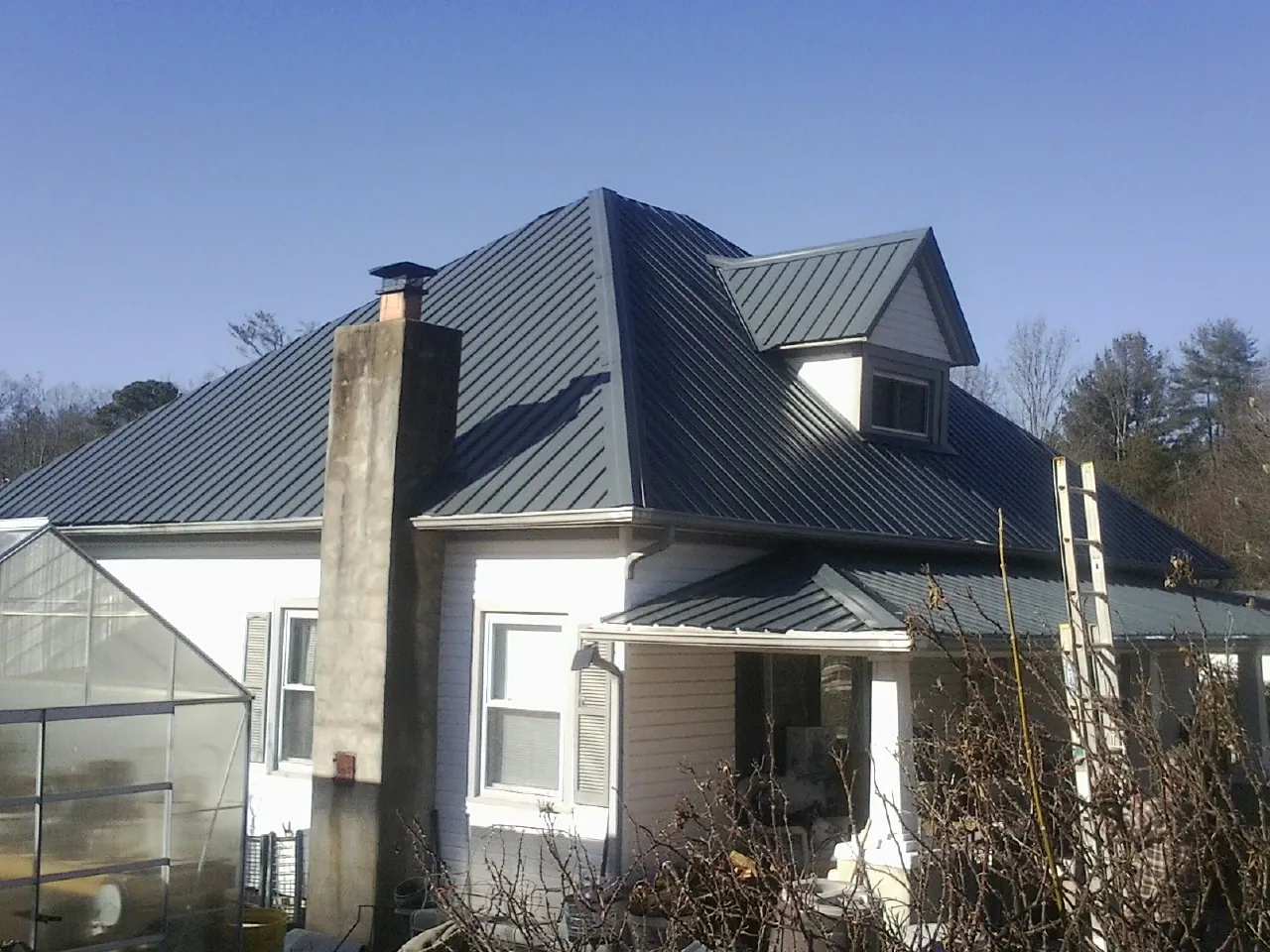 Dark blue standing seam metal roof on a white farmhouse with dormer — Slate & Tile Roof Repair by Roofing Brothers in North Pitcher
