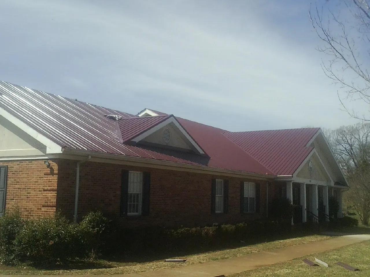 Red metal roof with gabled entries on a long brick building, from a Hail Damage Roof Repair job in North Pitcher