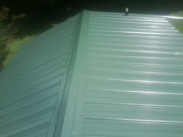 New green metal panels meeting at the ridge of a roof — Flat Roof Repair work by our crew in North Pitcher