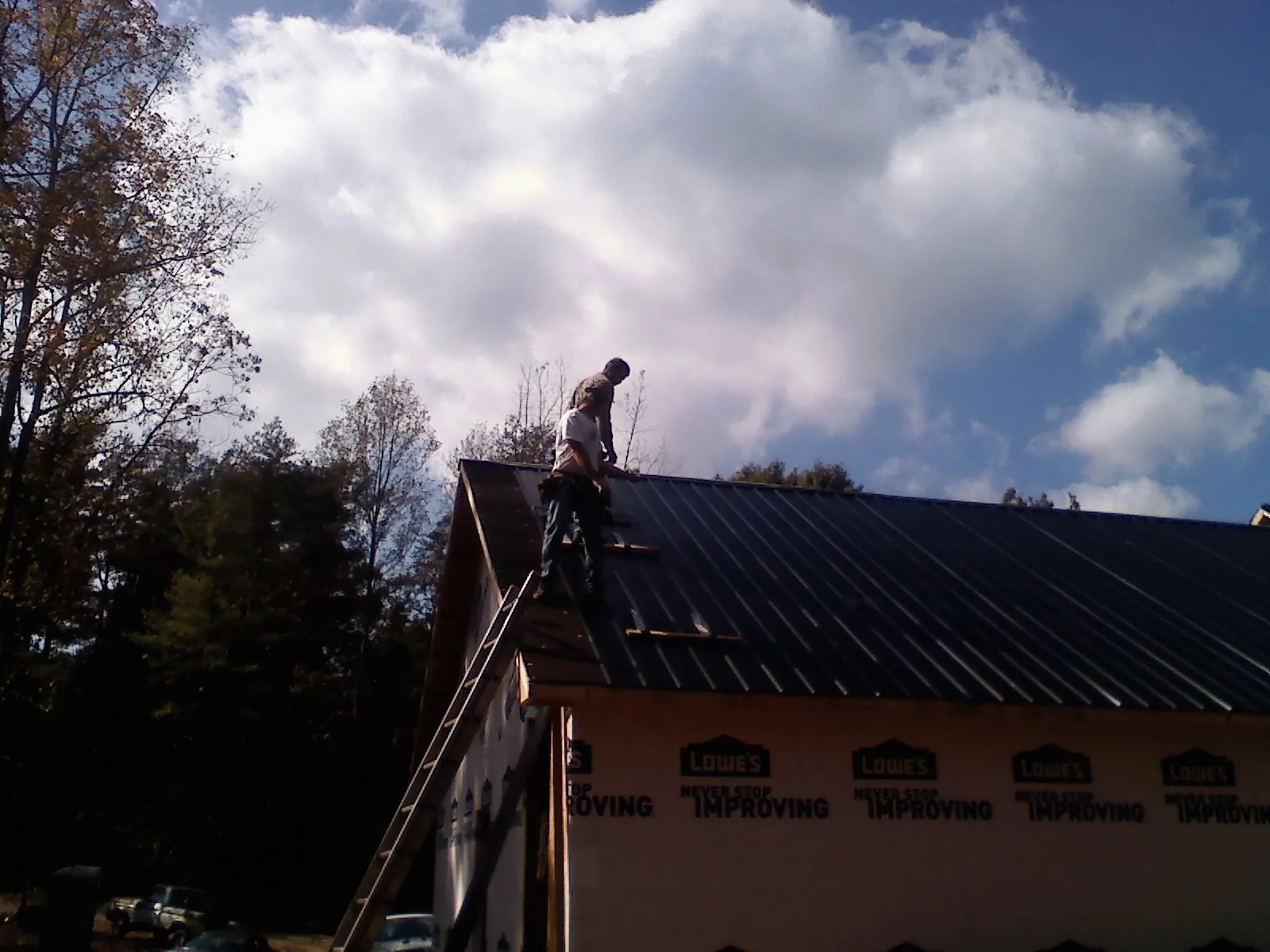 Roofer fastening dark metal panels high against a cloudy sky, from a Roof Inspection job in North Pitcher
