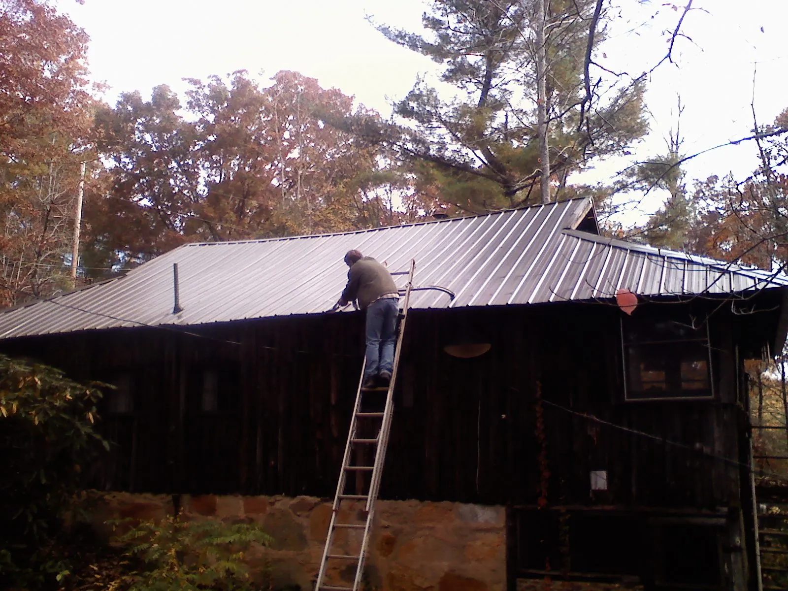 Roofer on a ladder working along the edge of a cabin metal roof in North Pitcher
