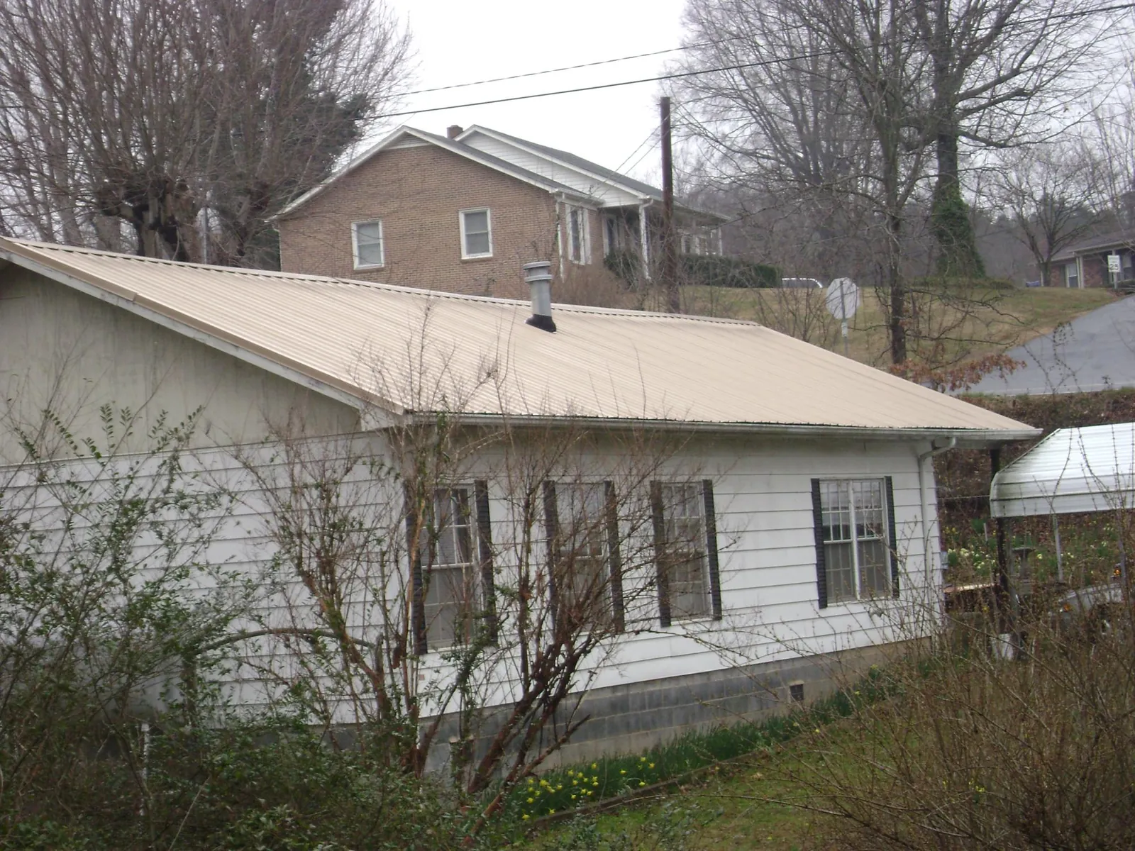 Tan metal roof on a white sided house set into a hillside — Commercial Roofing by Roofing Brothers in North Pitcher