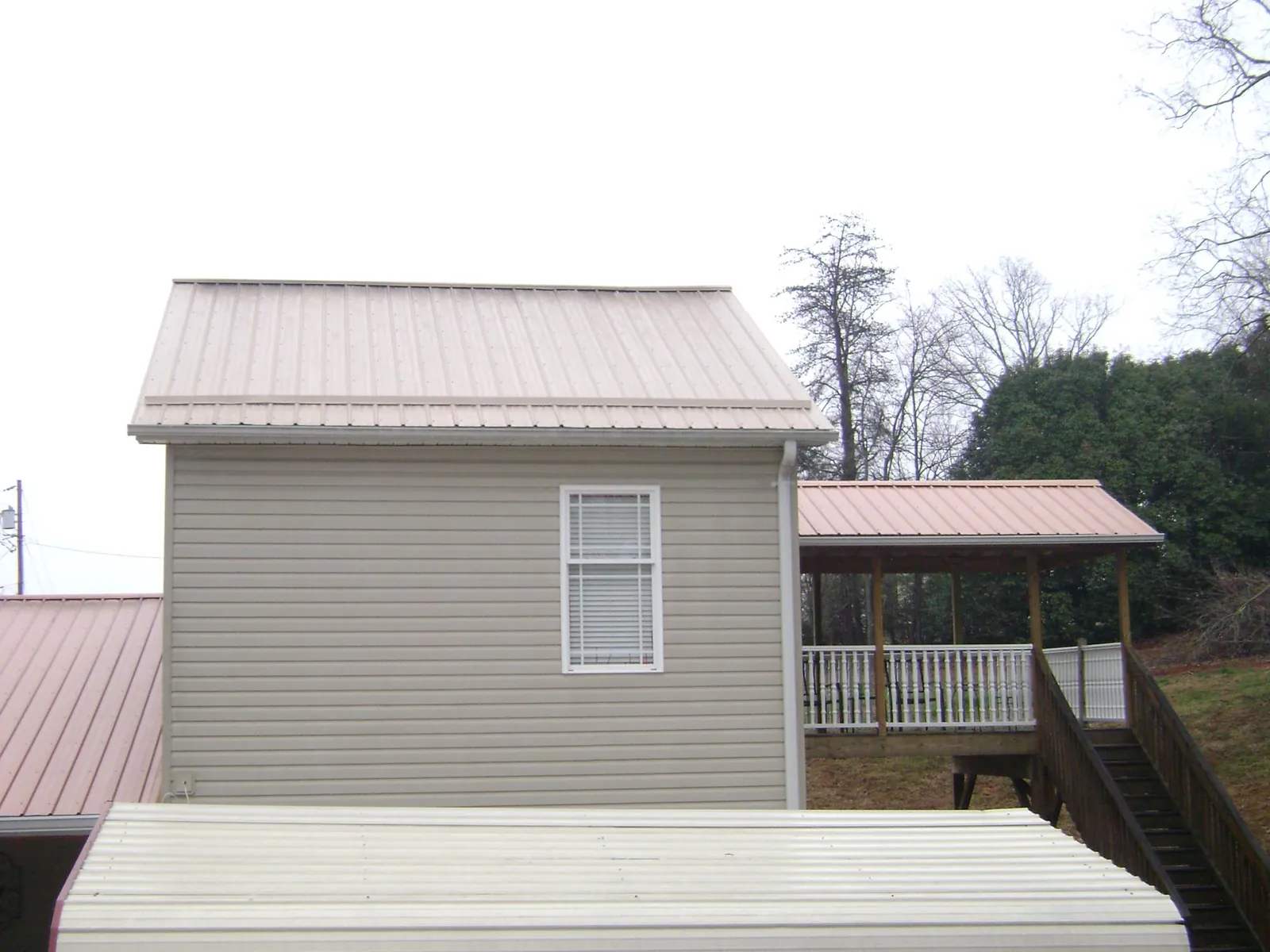 Tan metal roofs on a two story addition and attached porch, from a Roof Replacement job in North Pitcher